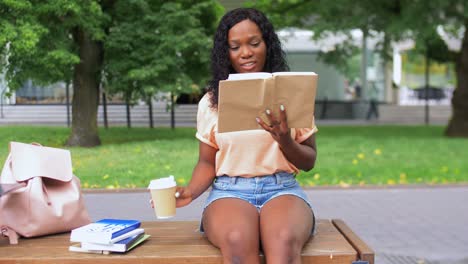 Chica-Estudiante-Leyendo-Un-Libro-Y-Tomando-Café.-Concepto-De-Educación,-Escuela-Y-Personas.-Chica-Estudiante-Afroamericana-Feliz-Y-Sonriente-Leyendo-Un-Libro-Y-Tomando-Café-Para-Llevar-En-La-Ciudad.